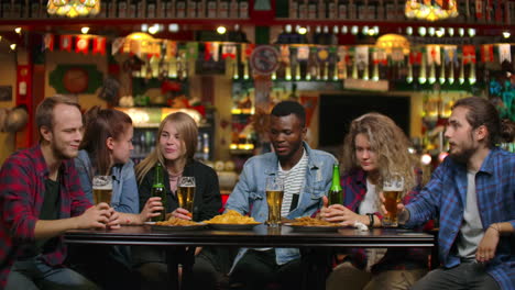Multi-ethnic-group-of-young-men-and-women-drinking-beer-at-a-bar-and-having-a-fun-discussion-about-the-university.